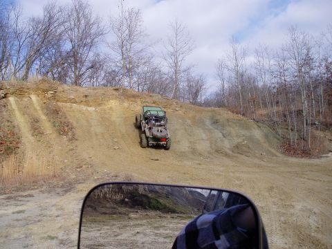 1992 Ford Bronco - An off-road vehicle navigates a steep dirt incline, with the reflection of another vehicle visible in the side mirror.