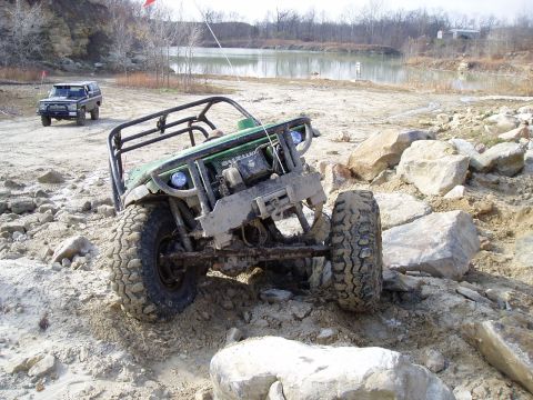 1992 Ford Bronco - An off-road buggy navigates a rocky terrain with a lake and trees in the background.