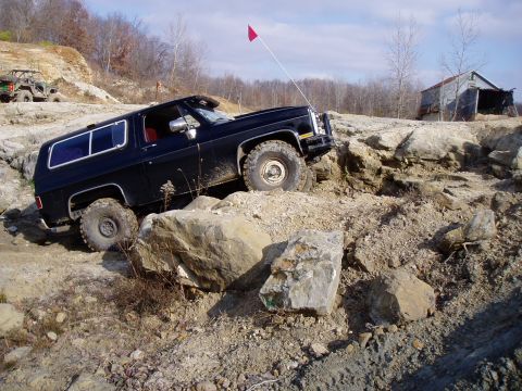 1992 Ford Bronco - An off-road SUV navigates a rocky terrain with a red flag on an antenna.