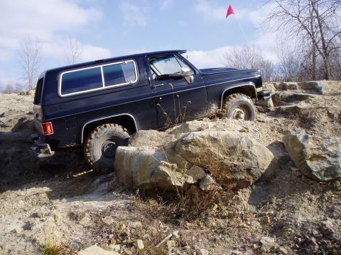 1992 Ford Bronco - A black SUV tackles a challenging off-road course with large rocks and dirt.