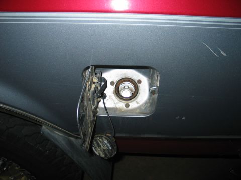 1995 Ford Bronco - The open fuel filler door reveals the metal housing and cap tethered to the body.