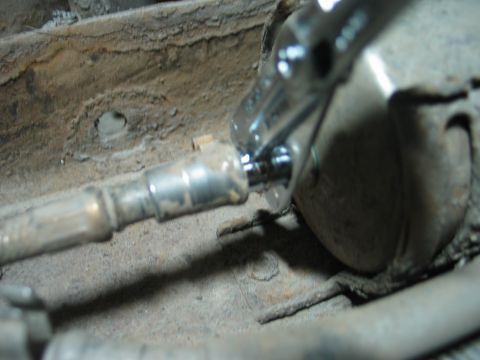 1995 Ford Bronco - A mechanic uses a wrench to remove a fuel filter, with visible rust on the vehicle's undercarriage.