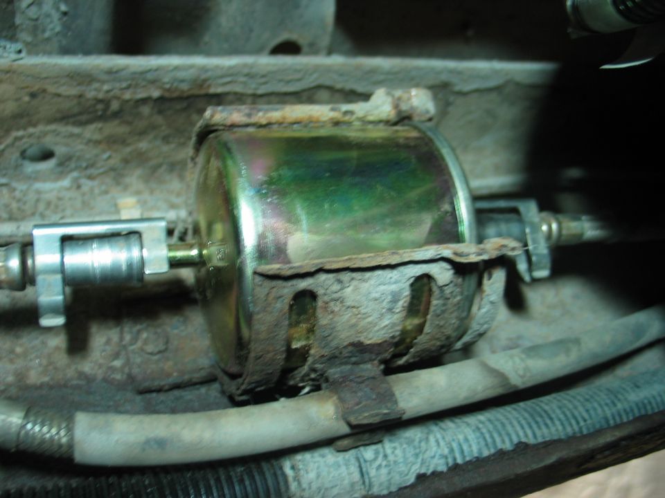 Gold inline fuel filter in rusty bracket with fuel line fittings