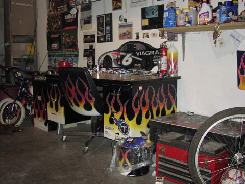 1981 Ford Bronco - A cluttered garage scene features a desk and chair adorned with flame graphics, a bicycle, and a red tool chest.