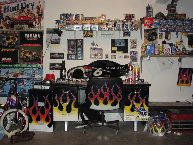 Garage interior with shelves of collectibles, a desk with flame decals, and a racing car graphic on the wall
