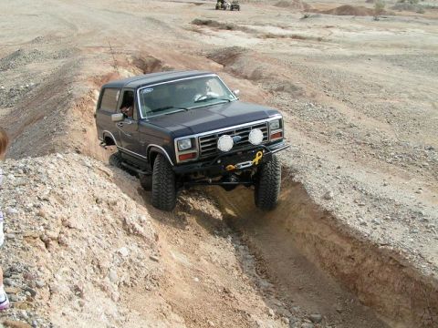 1985 Ford Bronco - This Ford Bronco navigates a challenging off-road trail in a desert-like environment.