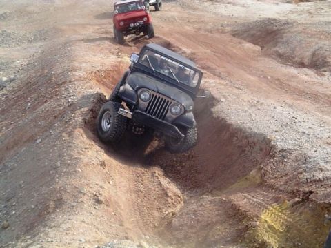 1985 Ford Bronco - Multiple off-road vehicles tackle challenging terrain on a dirt track.