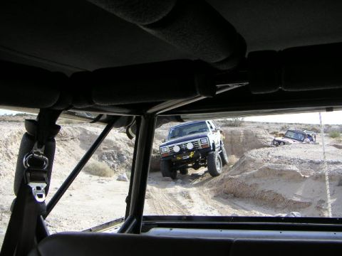 1985 Ford Bronco - Two modified SUVs are seen off-roading in a desert canyon, with one vehicle ascending a steep incline.