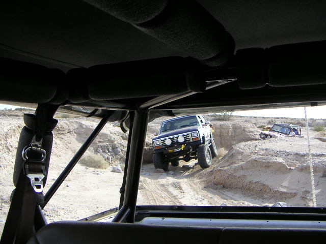 View from inside a vehicle of a white SUV climbing a sandy off-road dune