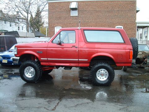 1994 Ford Bronco - Side view of a red lifted 1994 Ford Bronco with aftermarket wheels and tires.