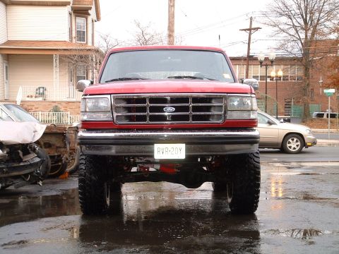 1994 Ford Bronco - A red 1994 Ford Bronco is parked on a wet street, facing the camera.