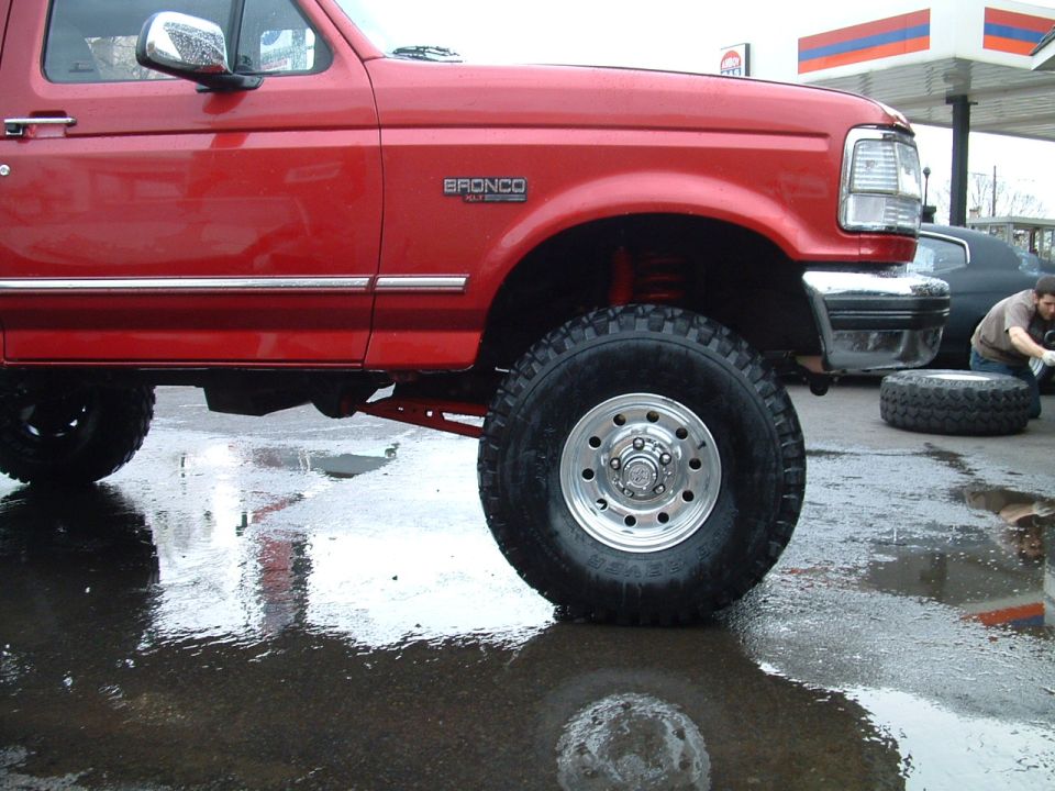 Red 1994 Ford Bronco with chrome trim and large tires, parked on wet pavement