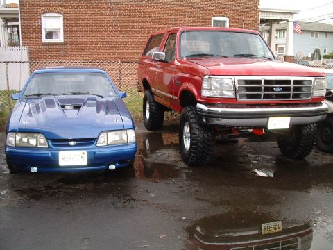 1994 Ford Bronco - A red 1994 Ford Bronco is parked next to a blue Ford Mustang, both vehicles are facing the camera.