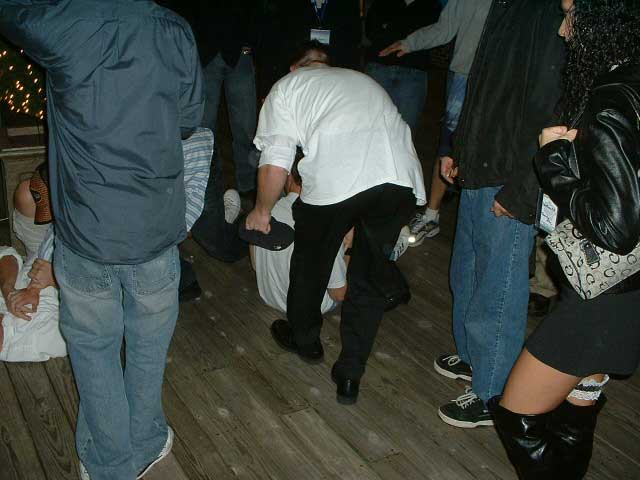 People are gathered indoors, some standing and some on the floor. One person is holding a black object