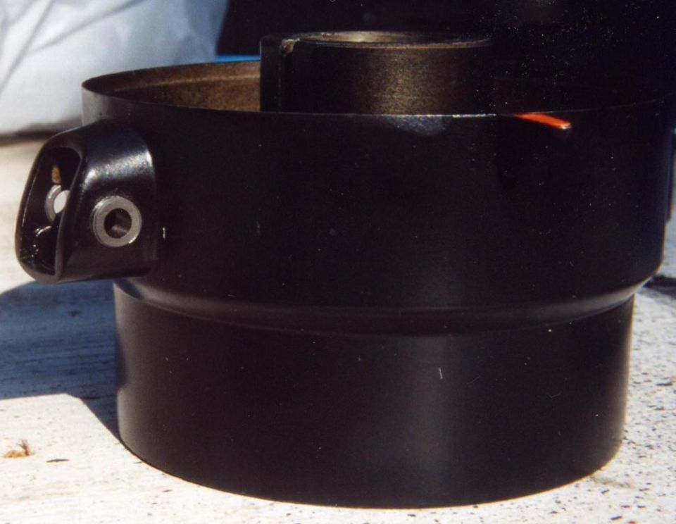 Black cylindrical car part with cast mounting ear and bushing hole, sitting on concrete