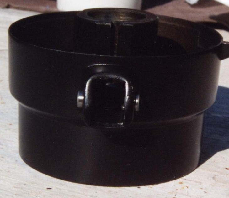 Black cylindrical column collar part with metal pivot bracket, photographed on weathered wood