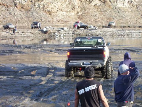 2000 Ford F-450 - Several trucks navigate a muddy terrain with a rocky hillside in the background.