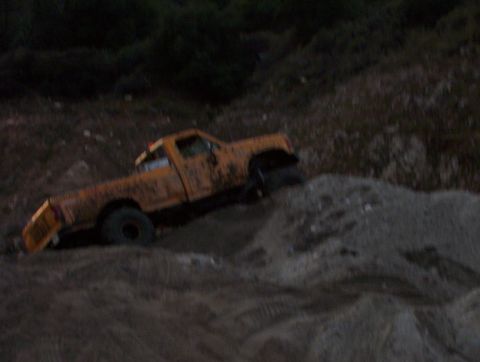 2000 Ford F-450 - An old orange pickup truck is seen driving up a steep dirt incline at dusk.