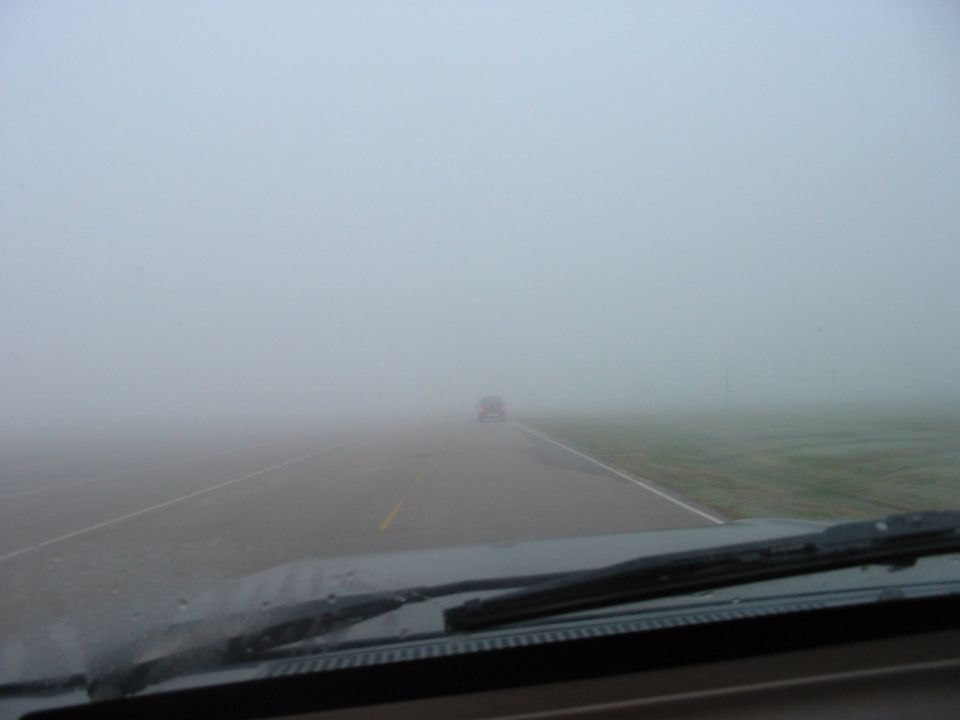 View from car interior looking out at a distant vehicle in heavy fog