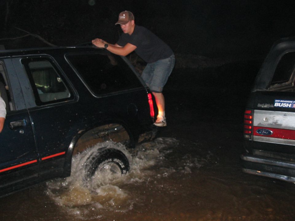guy climbing on SUV stuck in water, another SUV behind him