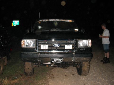 1988 Ford Bronco - A black Ford Bronco is parked at night, with a man standing to the side holding a drink.