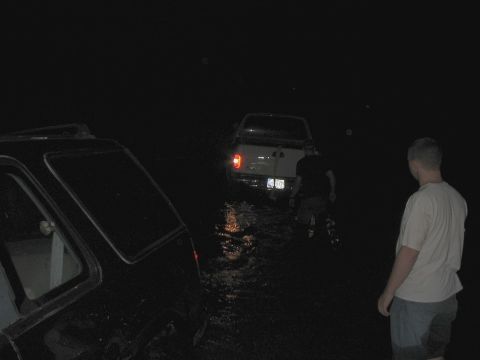 1988 Ford Bronco - Two trucks are stuck in water at night, with a person observing the scene.