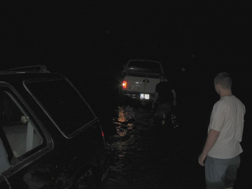 Two trucks partially submerged in water at night, with a person standing nearby