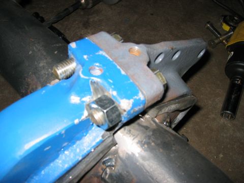 1978 Ford Bronco - Close-up of a blue-painted radius arm end where it bolts to a gray drop bracket on a truck front axle, showing the large radius-arm nut, th…
