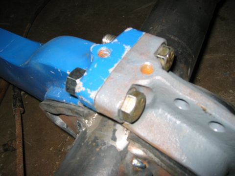 1978 Ford Bronco - Close-up of a blue-painted radius arm end bolted against a gray-primered wedge bracket on a black solid front axle tube; two hex bolts are…