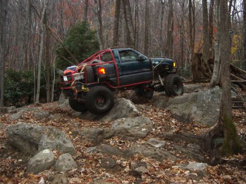 1985 Ford Bronco - Custom off-road truck navigating a rocky trail in a forest during autumn.