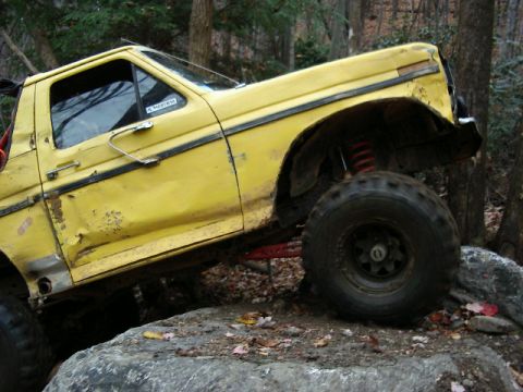 1985 Ford Bronco - This yellow truck, likely from the early 1980s, navigates a rocky trail with its off-road modifications.