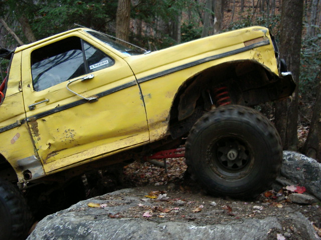 Yellow off-road truck with large tires and lifted suspension, angled on rocks