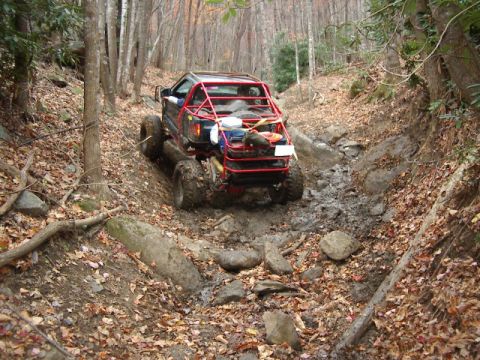 1985 Ford Bronco - This heavily modified off-road vehicle is tackling a challenging muddy and rocky trail.