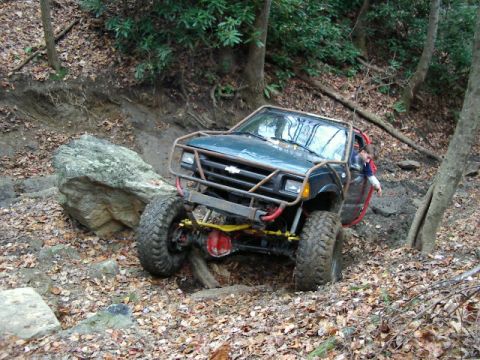 1985 Ford Bronco - This modified off-road vehicle navigates a challenging, rocky trail in a wooded area.