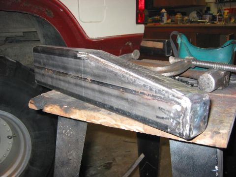 1985 Ford Bronco - A custom metal bumper is clamped to a workbench, with parts of a vehicle visible in the background.