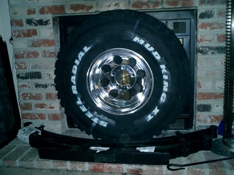 1990 Ford Bronco - A Mud King XT tire and a leaf spring are displayed in front of a brick fireplace.
