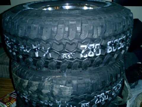 1990 Ford Bronco - Three off-road tires are stacked, showing white markings for size and possibly other identifiers.