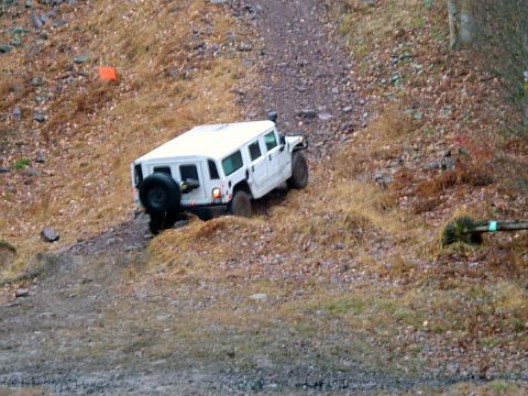1979 Ford Bronco - A white SUV navigates a steep, rocky incline covered in dry grass and loose stones.