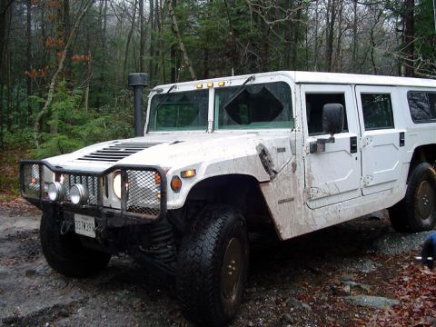 1979 Ford Bronco - A white Hummer H1 sits on a muddy dirt road, its windshield cracked, surrounded by trees.