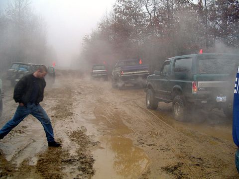 1979 Ford Bronco - A green SUV navigates a muddy track with other vehicles in the background, kicking up dust and mist.