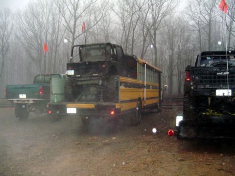 1979 Ford Bronco - Multiple modified vehicles, including a school bus carrying a jeep, are parked outdoors on a misty day.