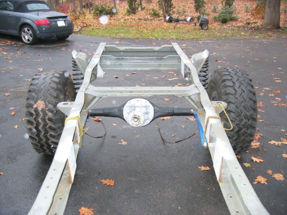 Bare Ford Bronco rolling chassis frame with rear axle and mud tires in driveway