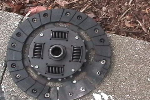 1996 Ford Bronco - A worn clutch disc and pressure plate assembly lies on a textured surface with scattered leaves and mulch.
