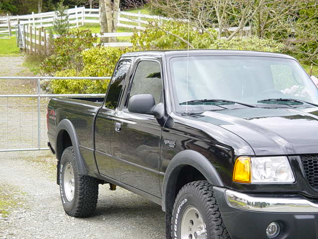 Black 2003 Ford Ranger pickup truck parked on gravel near a white fence