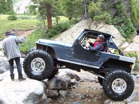 1991 Ford Bronco - A Jeep Wrangler tackles a challenging rocky trail with a driver and passenger observing.