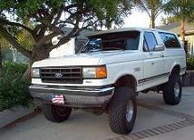 1988 Ford Bronco - This lifted white Ford Bronco sits on a paved driveway, its front end angled towards the camera.