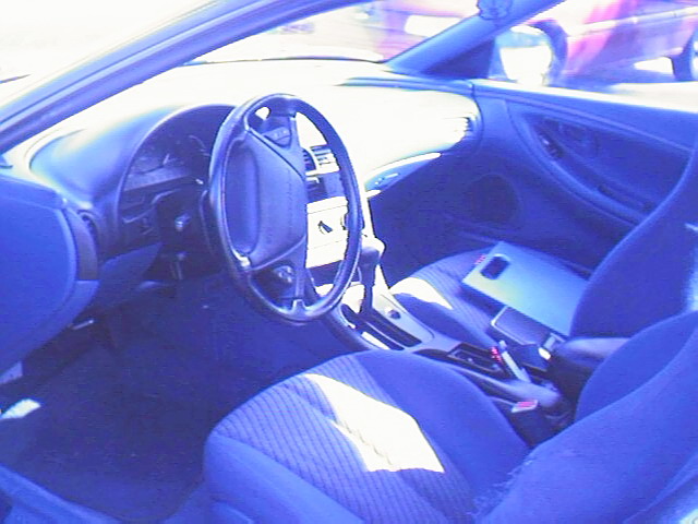 Car interior with steering wheel, dash, cloth seats and automatic shifter, blue-tinted.