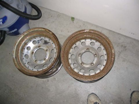 1987 Ford Bronco - Two rusty steel wheels are shown on a concrete floor next to a shop vac.