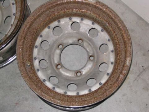 1987 Ford Bronco - Close-up of a rusty steel wheel, showing its circular pattern of lug nut holes and signs of wear.