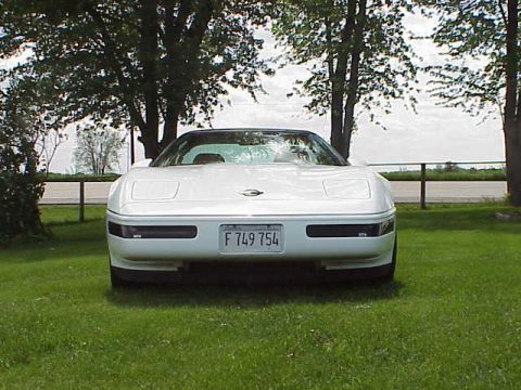 1994 Chevrolet Corvette - A white 1994 Chevrolet Corvette is seen from the front, parked on a grassy area with trees in the background.